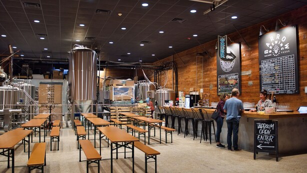 A taproom with wooden tables and stools, a bar area, and brewing equipment.