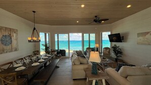 A spacious living area with a long dining table, comfortable seating, and a view of the ocean.