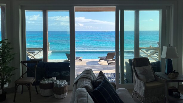 A room with a view of the ocean through large glass doors, a wicker sofa, a chair, and a lamp.