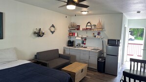 Ein kompakter Raum mit Bett, Schlafsofa, Couchtisch, Küchenzeile mit Mikrowelle, Kühlschrank und Esstisch.