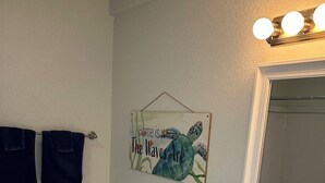Ein Badezimmer mit Toilette, Waschbecken und Spiegel. Handtuchhalter mit Handtüchern, Toilettenpapierhalter und ein dekoratives Schild an der Wand.
