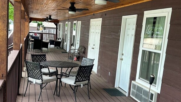 Eine überdachte Terrasse mit Holzdeck, einem Tisch und Stühlen sowie einem Deckenventilator.