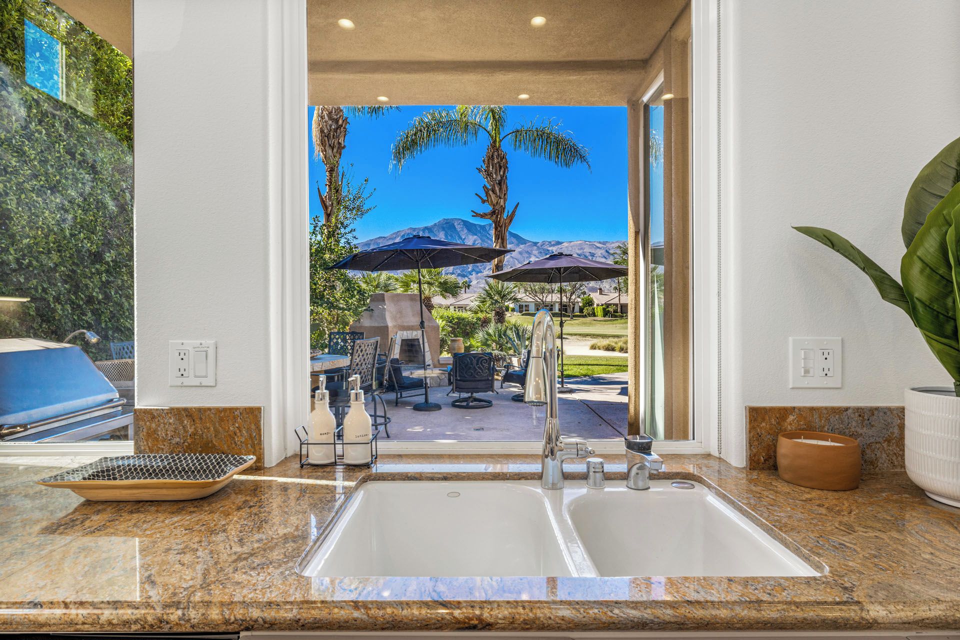 A kitchen with granite countertops, a double sink, and a view of an outdoor patio with umbrellas and chairs.