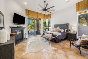 Un dormitorio amplio con una cama grande, ventilador de techo, chimenea y vistas al exterior.