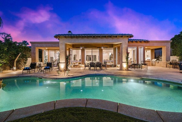 Una casa grande con piscina, mobiliario exterior y un patio cubierto.