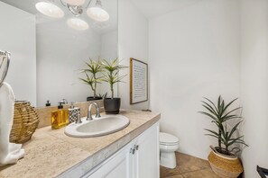 Un baño moderno con lavamanos, espejo e inodoro. Hay dos plantas en maceta en el mueble y otra en el suelo.