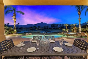 An outdoor dining area with a view of a mountain range and a pool at dusk. - Bella Vida - 4000 PGA West Villa (La Quinta)