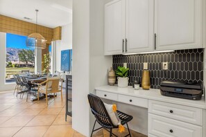 Una cocina moderna con armarios blancos, salpicadero de azulejos negros y un comedor con vistas a montañas.