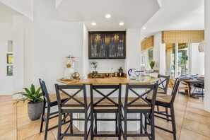 A modern kitchen with a central island, dark chairs, and a dining area with a view of the outdoors. - Bella Vida - 4000 PGA West Villa (La Quinta)