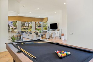 A pool table with balls and cues, a sofa, chairs, a TV, and a window with a view of palm trees. - Bella Vida - 4000 PGA West Villa (La Quinta)