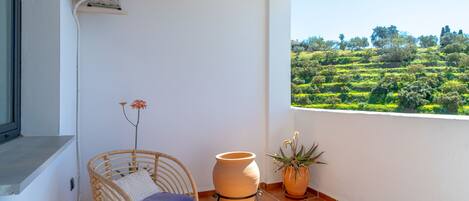 A balcony with wicker chairs, a large terracotta pot, and a view of a green landscape.