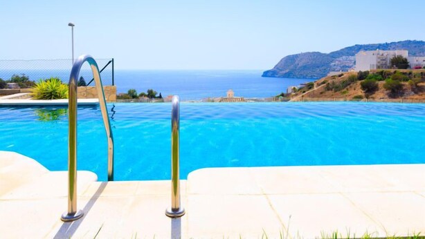 A swimming pool with clear blue water, a metal ladder, and a view of the sea and a hillside with buildings. - Vacation home Melon by Interhome (La Herradura)