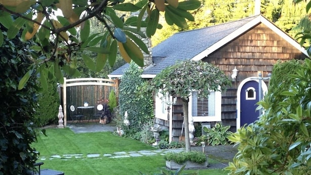 Un jardin bien entretenu avec une maison en bois, un patio couvert et un petit coin salon.
