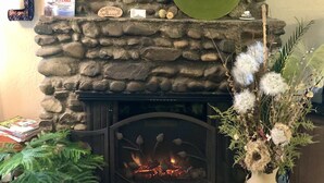 Une cheminée en pierre surmontée d’une plaque de verre verte, un pot de fleurs et un vase rempli de fleurs blanches.