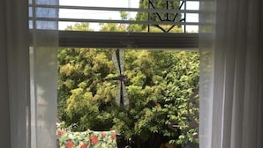 Une fenêtre donnant sur un jardin aménagé avec du mobilier d’extérieur et une végétation luxuriante.
