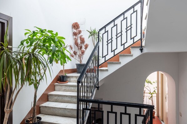 A staircase with a black railing, potted plants, and a view of a courtyard. - Domus Sicile - Panormus Cala a Mare (Palermo)