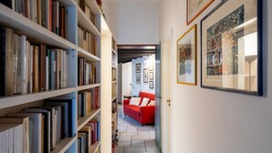 A narrow hallway with bookshelves on both sides, a red sofa in the distance, and framed artwork on the walls.