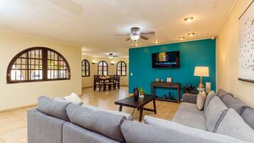 A spacious living area with a teal accent wall, a flat-screen TV, and a dining area with a table and chairs.