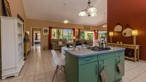 A spacious kitchen with a central island, a dining area with a sofa, and a view of the outdoors through large windows. - Spacious 5BR Home w/ Amazing Garden & PrivatePool (Noord)