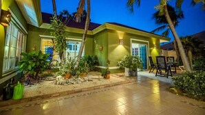 A well-lit house with a tiled patio, surrounded by palm trees and potted plants. - Spacious 5BR Home w/ Amazing Garden & PrivatePool (Noord)