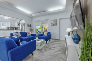 A modern living room with blue sofas, a coffee table, and a TV on a white console.