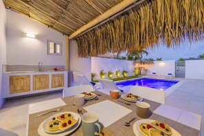 Un espace repas avec une piscine, une cuisine et un toit de chaume.