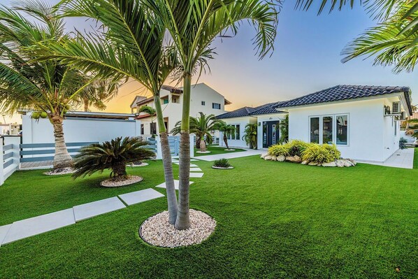 A modern house with a well-maintained lawn, palm trees, and a clear sky.