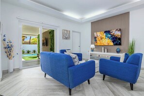 Un salon moderne avec deux canapés bleus, un téléviseur à écran plat et une porte-fenêtre coulissante donnant sur un balcon.