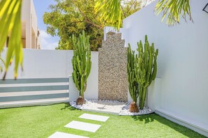 Un espace extérieur moderne avec une pelouse artificielle, des dalles de pierre blanche et de grands cactus.