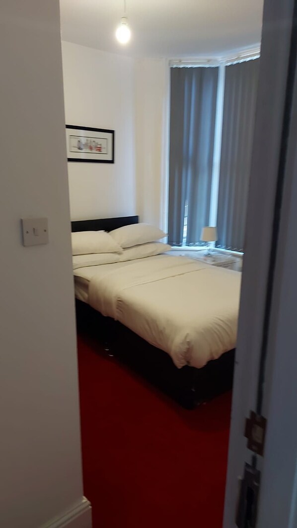 A hotel room with a bed, a window with curtains, a wall-mounted light, and a framed picture. - Midtown Guesthouse (Liverpool)