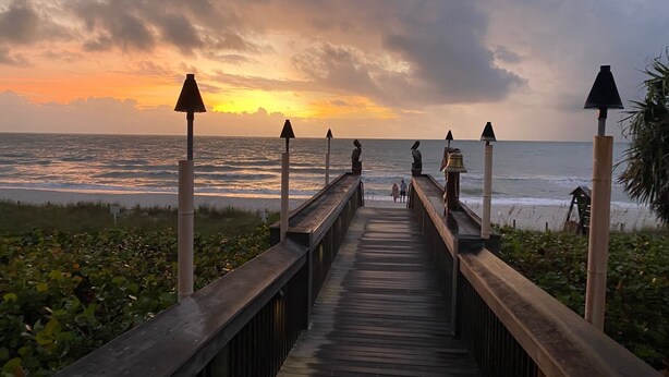 A wooden boardwalk leading to the beach with lamp posts and a view of the ocean at sunset. -  **GEM!**3 BR BEACH HOUSE w/ HEATED POOL, short ride to the beach!  (Naples)