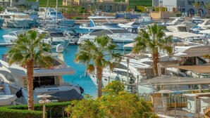A marina with multiple yachts docked, surrounded by palm trees and modern buildings. - VESTA - Superior APT - 3BR - New Marina (El Gouna)