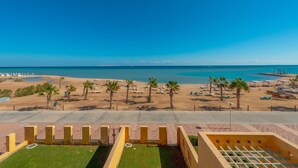 A beach resort with a clear view of the ocean, palm trees, and a paved walkway leading to the beach. - VESTA - Superior APT - 3BR - New Marina (El Gouna)