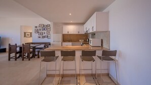 A modern kitchen with white cabinets, a central island, and bar stools. - VESTA - Superior APT - 3BR - New Marina (El Gouna)