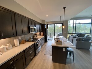 A modern kitchen with dark cabinetry, a central island, and a large window overlooking a deck.