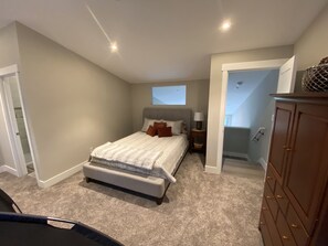 A bedroom with a bed, nightstand, and dresser. There is a window above the bed and a door leading to another room.