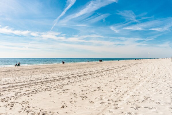 Une vaste plage de sable fin parsemée d’empreintes, un ciel dégagé et une mer calme.