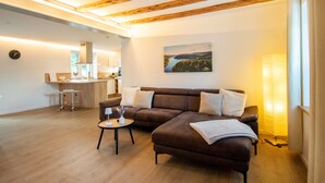 A modern living room with a brown sofa, a small round table, and a kitchen area in the background. - Holiday Home 'Traumzeit' with Private Terrace, Private Garden and Wi-Fi (Neuhütten)