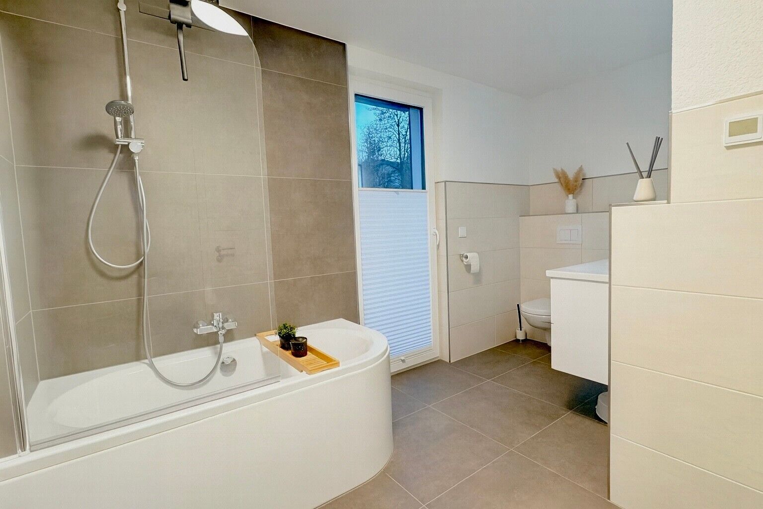 Ein modernes Badezimmer mit Badewanne, Dusche, Toilette und einem Fenster mit Blick auf Bäume.
