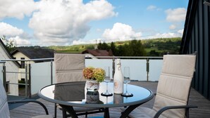 A round table with chairs on a balcony, a vase with flowers, and two wine glasses. - Holiday Home 'Traumzeit' with Private Terrace, Private Garden and Wi-Fi (Neuhütten)