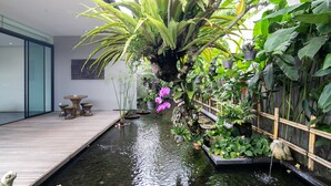 Ein ruhiger Innenbereich mit einem Garten, einer Wasserattraktion, einem Holzboden und verschiedenen Blumentöpfen.
