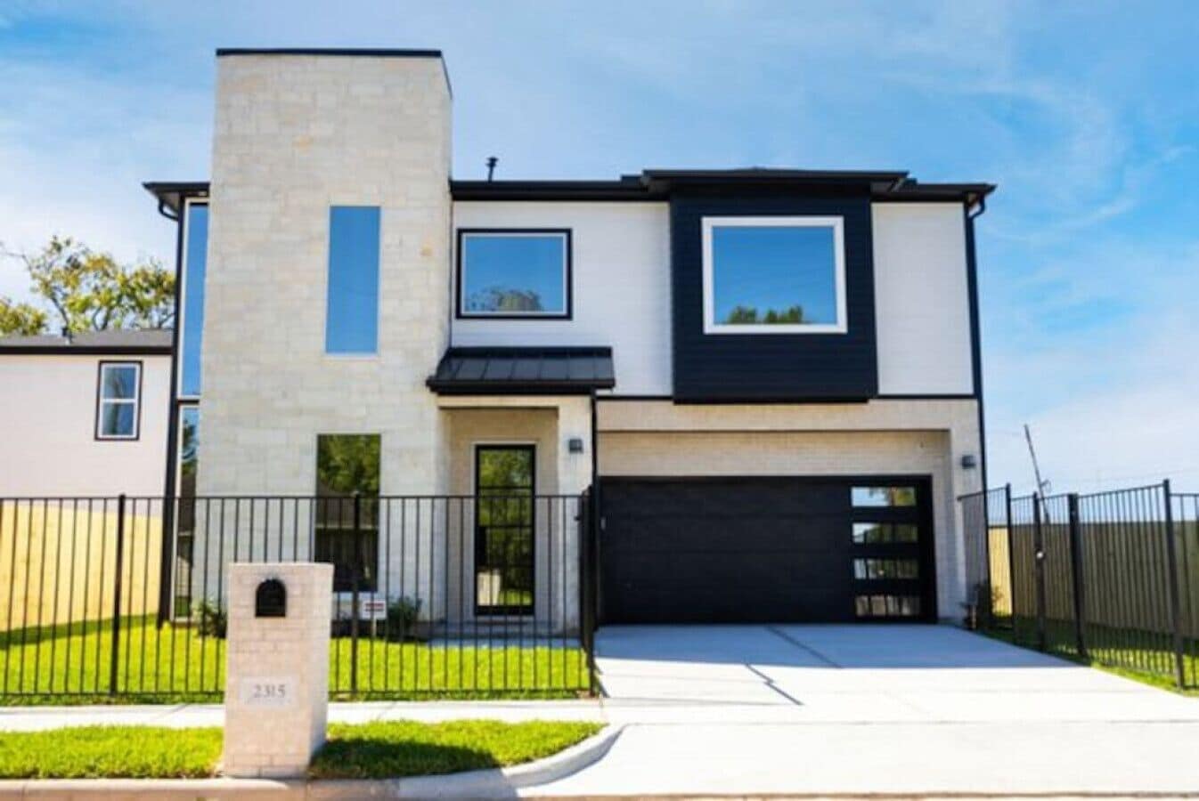 Una casa moderna a due piani con garage, un pilastro in pietra e un prato curato.