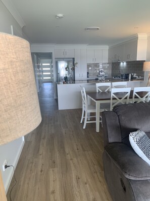 A modern kitchen with white cabinets, a central island, and a dining area with white chairs.