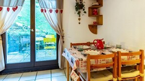 A dining area with a table set for four, a red pitcher, and a wooden shelf with decorative items.