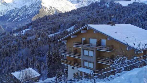 A chalet with a wooden exterior, multiple balconies, and a view of snow-covered mountains.