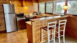 A kitchen with wooden walls, a stainless steel refrigerator, a microwave, an oven, a sink, and wooden bar stools. - Perfect Waterfront Escape in Marlo | Balcony Views & Nature All Around (Marlo)