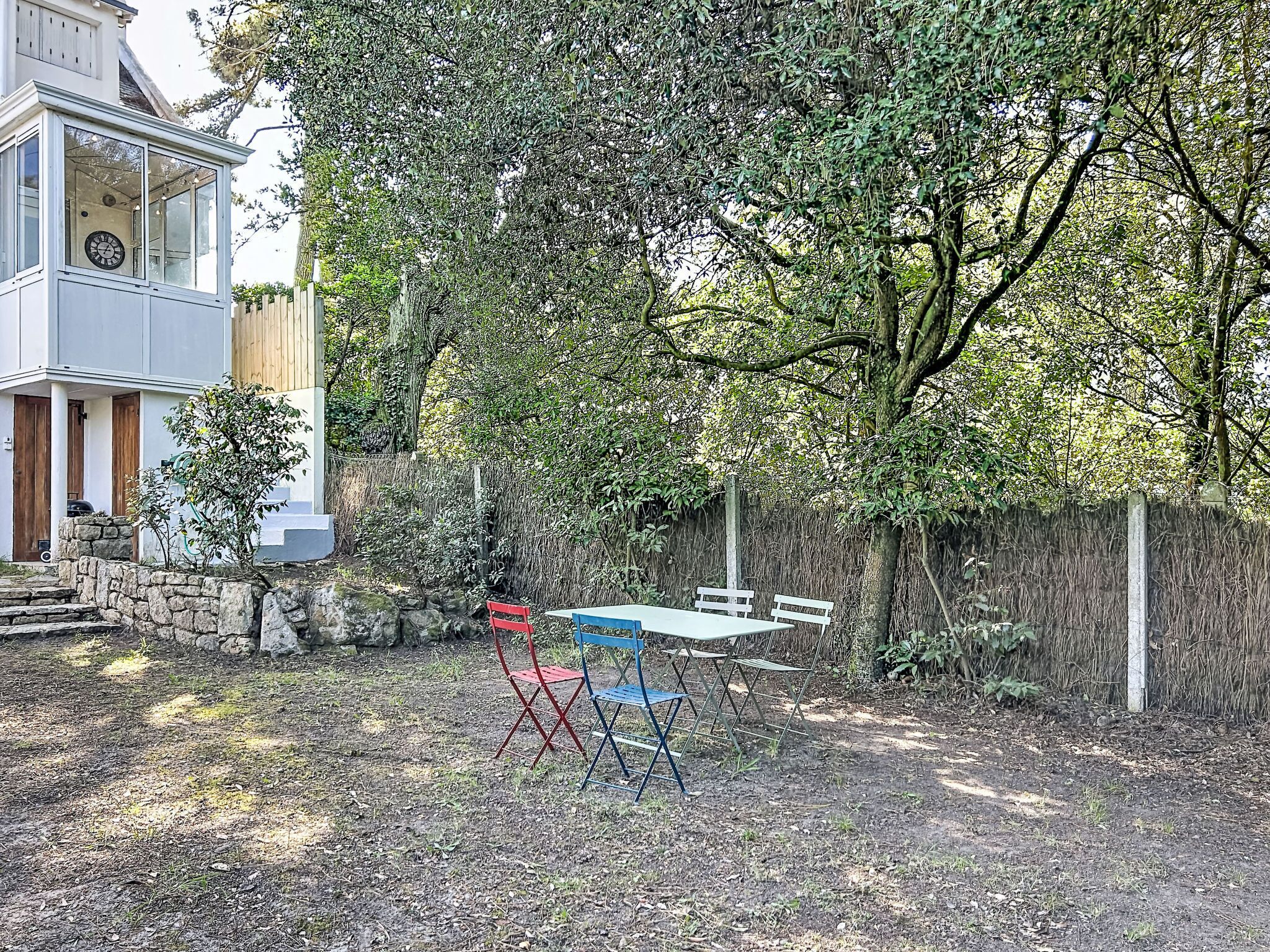 A backyard with a stone wall, a wooden fence, and a table with chairs.
