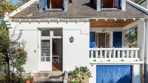 Ein zweistöckiges Haus mit weißer Fassade, einem Balkon mit weißen Geländern und einer blauen Garagentür.