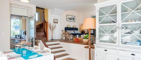 Amplia sala de estar con una mesa de comedor dispuesta para cuatro personas, una escalera que conduce a otro nivel y un mueble blanco con puertas de vidrio.