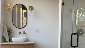 A bathroom with a white sink, round mirror, and a glass shower enclosure. - Historic • Hot tub • A&M Ring Day (Bryan)